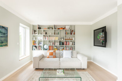 Inspiration pour un salon beige et blanc design de taille moyenne et ouvert avec une bibliothèque ou un coin lecture, un mur vert, parquet clair et un téléviseur fixé au mur.