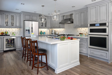 Inspiration for a large transitional l-shaped medium tone wood floor and beige floor eat-in kitchen remodel in Other with a double-bowl sink, raised-panel cabinets, gray cabinets, quartz countertops, white backsplash, porcelain backsplash, stainless steel appliances and an island