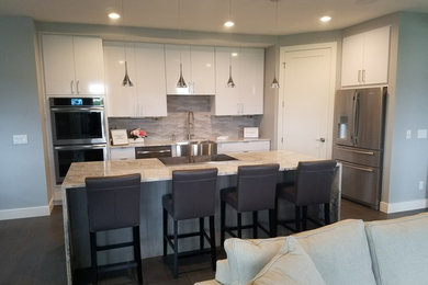Inspiration for a modern l-shaped gray floor open concept kitchen remodel in Other with a farmhouse sink, flat-panel cabinets, white cabinets, white backsplash, stainless steel appliances, an island, multicolored countertops and quartz countertops