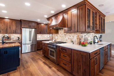 Design ideas for a large eat-in kitchen in Denver with dark wood cabinets, stainless steel appliances, brown floor, white benchtop, a farmhouse sink, travertine splashback, with island, recessed-panel cabinets, multi-coloured splashback, dark hardwood floors and quartzite benchtops.