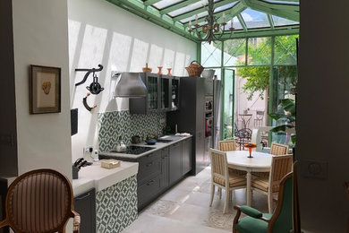 Large transitional single-wall open plan kitchen in Marseille with a farmhouse sink, shaker cabinets, dark wood cabinets, granite benchtops, green splashback, cement tile splashback, black appliances, cement tiles, beige floor and grey benchtop.