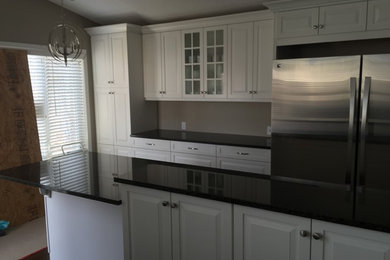 Inspiration for a mid-sized transitional single-wall eat-in kitchen remodel in Calgary with raised-panel cabinets, white cabinets, solid surface countertops, stainless steel appliances and an island