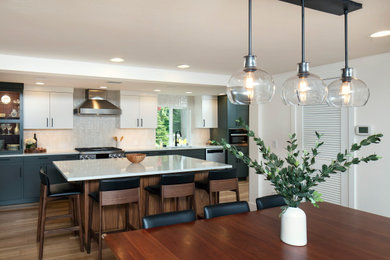 Example of a mid-sized trendy galley medium tone wood floor eat-in kitchen design in Seattle with an undermount sink, recessed-panel cabinets, quartz countertops, white backsplash, ceramic backsplash, stainless steel appliances, an island and white countertops