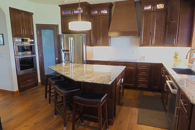 This is an example of a large traditional l-shaped kitchen/diner in Denver with a submerged sink, shaker cabinets, dark wood cabinets, granite worktops, white splashback, ceramic splashback, stainless steel appliances, vinyl flooring, an island, brown floors and multicoloured worktops.