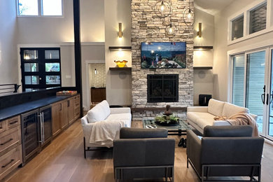 Living room - mid-sized contemporary open concept light wood floor, brown floor and exposed beam living room idea in Seattle with gray walls, a standard fireplace, a stacked stone fireplace and a wall-mounted tv