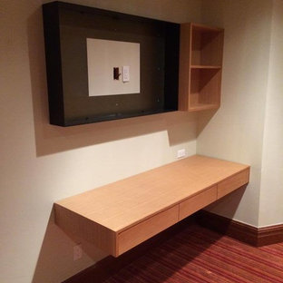 This is an example of a medium sized modern study in Denver with beige walls, carpet, a built-in desk and red floors.