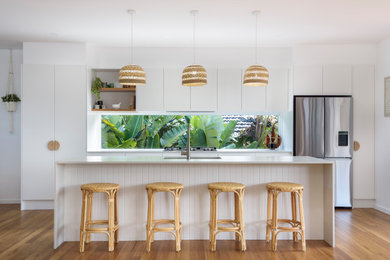 This is an example of a small beach style galley eat-in kitchen in Newcastle - Maitland with an undermount sink, flat-panel cabinets, white cabinets, quartz benchtops, white splashback, window splashback, stainless steel appliances, with island and white benchtop.