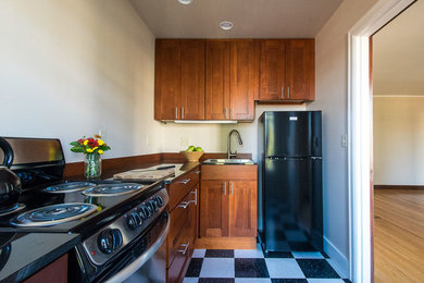 Example of a mid-sized mountain style l-shaped porcelain tile and multicolored floor enclosed kitchen design in Seattle with a drop-in sink, recessed-panel cabinets, dark wood cabinets, granite countertops, black appliances and no island