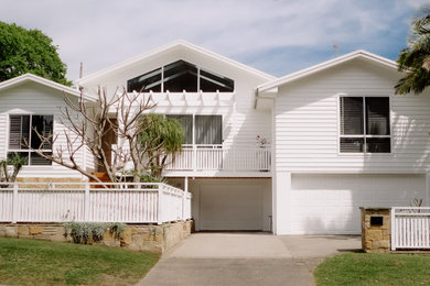 This is an example of a large beach style two-storey white house exterior in Central Coast with concrete fiberboard siding, a gable roof, a metal roof, a white roof and board and batten siding.