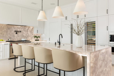Kitchen pantry - large transitional l-shaped limestone floor and beige floor kitchen pantry idea in Orange County with an undermount sink, white cabinets, quartzite countertops, white backsplash, stone slab backsplash, paneled appliances, an island and white countertops