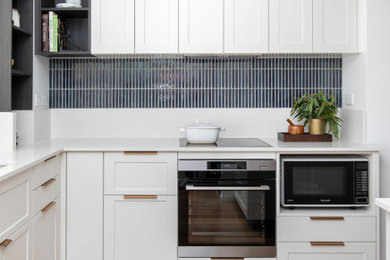Photo of a transitional l-shaped kitchen in Brisbane with shaker cabinets, white cabinets, quartz benchtops, blue splashback, porcelain splashback, brown floor and white benchtop.