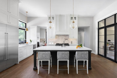 Diseño de cocina clásica renovada grande abierta con salpicadero blanco, electrodomésticos de acero inoxidable, una isla, suelo marrón y encimeras blancas
