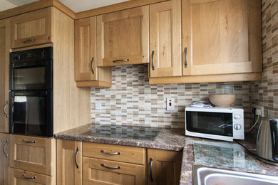 Mid-sized traditional l-shaped eat-in kitchen in Other with a drop-in sink, recessed-panel cabinets, medium wood cabinets, granite benchtops, multi-coloured splashback, mosaic tile splashback, black appliances, porcelain floors and multi-coloured floor.