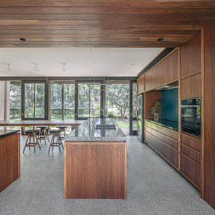 Photo of a midcentury l-shaped eat-in kitchen in Sydney with an undermount sink, flat-panel cabinets, medium wood cabinets, black appliances, with island, grey floor and grey benchtop.