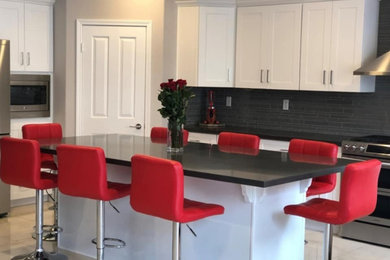 Large minimalist l-shaped gray floor kitchen photo in Orange County with shaker cabinets, white cabinets, solid surface countertops, black backsplash, porcelain backsplash, stainless steel appliances, an island and black countertops