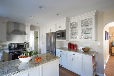 Inspiration for a mid-sized cottage u-shaped medium tone wood floor and brown floor kitchen remodel in Chicago with an undermount sink, recessed-panel cabinets, white cabinets, granite countertops, white backsplash, subway tile backsplash, stainless steel appliances and a peninsula