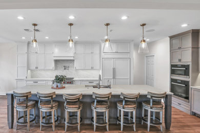 Large transitional l-shaped open plan kitchen in Jacksonville with an undermount sink, recessed-panel cabinets, medium wood cabinets, marble benchtops, white splashback, marble splashback, panelled appliances, vinyl floors, with island, brown floor and white benchtop.