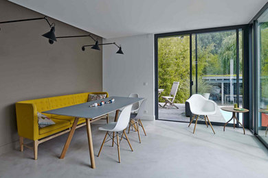 Cette photo montre une grande salle à manger ouverte sur le salon moderne avec un mur gris, sol en béton ciré, aucune cheminée et un sol gris.