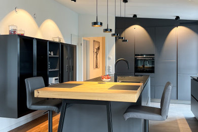 Offene, Einzeilige, Geräumige Moderne grifflose Küche mit flächenbündigen Schrankfronten, schwarzen Schränken, dunklem Holzboden und Kücheninsel in Hamburg