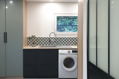 Idées déco pour une grande buanderie industrielle multi-usage avec un évier encastré, des portes de placards vertess, un plan de travail en bois, un mur blanc, un sol en carrelage de céramique, des machines côte à côte et un sol gris.