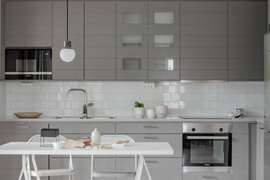 Photo of a scandinavian l-shaped eat-in kitchen in Orebro with an undermount sink, grey cabinets, white splashback, subway tile splashback, stainless steel appliances, light hardwood floors, no island and white benchtop.