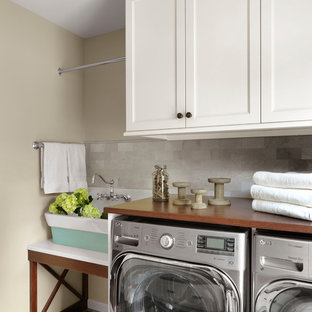 Inspiration for a farmhouse single-wall separated utility room in St Louis with a belfast sink, shaker cabinets, white cabinets, wood worktops, beige walls, painted wood flooring, a side by side washer and dryer, multi-coloured floors and brown worktops.