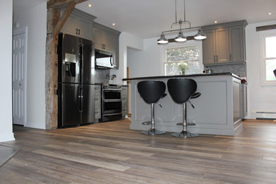 Inspiration for a mid-sized transitional l-shaped vinyl floor and beige floor open concept kitchen remodel in Toronto with beaded inset cabinets, gray cabinets, mosaic tile backsplash, black appliances, an island, an undermount sink and gray backsplash