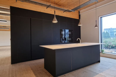 Inspiration for a large modern single-wall kitchen/diner in Other with an integrated sink, flat-panel cabinets, black cabinets, composite countertops, black appliances, light hardwood flooring, an island, beige floors, white worktops and a wood ceiling.