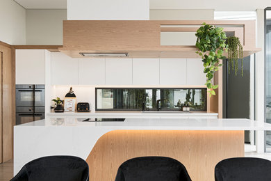 Design ideas for a large modern l-shaped eat-in kitchen in Perth with an undermount sink, recessed-panel cabinets, light wood cabinets, solid surface benchtops, white splashback, stone slab splashback, black appliances, porcelain floors, with island, grey floor and white benchtop.