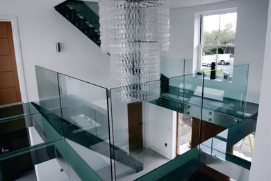 Large minimalist glass u-shaped metal railing and wall paneling staircase photo in Toronto