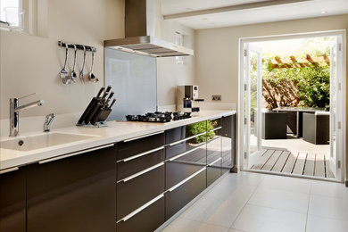 Design ideas for a large contemporary galley kitchen in London with a built-in sink, flat-panel cabinets, brown cabinets, composite countertops, blue splashback, glass sheet splashback, integrated appliances and porcelain flooring.