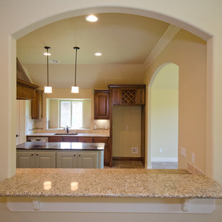 Large transitional kitchen pantry appliance - Kitchen pantry - large transitional galley ceramic floor kitchen pantry idea in Oklahoma City with a farmhouse sink, raised-panel cabinets, dark wood cabinets, granite countertops, beige backsplash, stone tile backsplash, stainless steel appliances and an island
