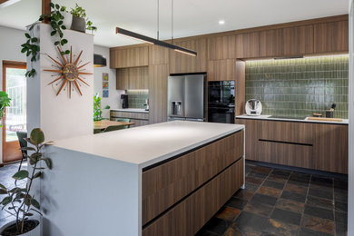 Inspiration for a mid-sized midcentury open plan kitchen in Perth with an undermount sink, medium wood cabinets, quartz benchtops, green splashback, stone tile splashback, black appliances, slate floors, with island, multi-coloured floor and white benchtop.