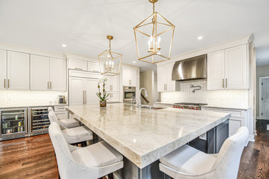 Large transitional l-shaped medium tone wood floor kitchen photo in New York with an undermount sink, shaker cabinets, white cabinets, quartzite countertops, white backsplash, marble backsplash, paneled appliances, an island and beige countertops