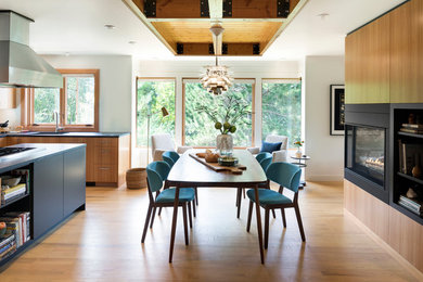 This is an example of a mid-sized kitchen/dining combo in Minneapolis with white walls, medium hardwood floors, a two-sided fireplace, a wood fireplace surround and beige floor.
