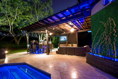 Expansive traditional backyard patio in Miami with an outdoor kitchen, natural stone pavers and a pergola.