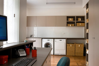 Design ideas for a large single-wall utility room in Brisbane with a single-bowl sink, beige cabinets, laminate benchtops, white walls, medium hardwood floors, a side-by-side washer and dryer and grey benchtop.