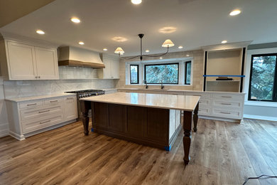 Example of a large country l-shaped laminate floor and brown floor eat-in kitchen design in Detroit with a drop-in sink, shaker cabinets, white cabinets, quartzite countertops, white backsplash, ceramic backsplash, stainless steel appliances, an island and white countertops