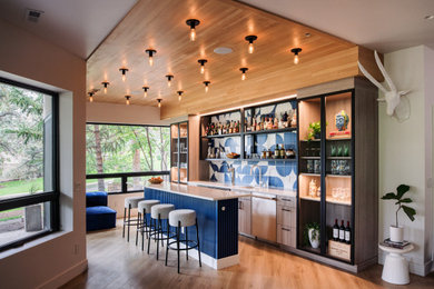 Example of a trendy galley medium tone wood floor and brown floor home bar design in Denver with an undermount sink, flat-panel cabinets, light wood cabinets, blue backsplash and white countertops