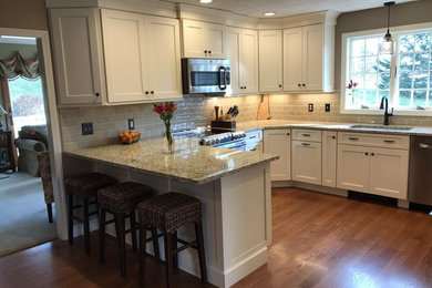 Transitional u-shaped medium tone wood floor eat-in kitchen photo in Boston with an undermount sink, shaker cabinets, white cabinets, granite countertops, beige backsplash, subway tile backsplash, stainless steel appliances and a peninsula