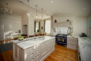 Mid-sized traditional u-shaped eat-in kitchen in Melbourne with a farmhouse sink, shaker cabinets, beige cabinets, marble benchtops, white splashback, stone slab splashback, coloured appliances, light hardwood floors and with island.