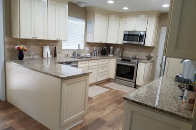 Large transitional u-shaped medium tone wood floor and brown floor enclosed kitchen photo in Tampa with a double-bowl sink, shaker cabinets, white cabinets, granite countertops, beige backsplash, stone tile backsplash, stainless steel appliances and a peninsula