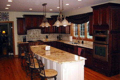 Inspiration for a mid-sized timeless l-shaped medium tone wood floor kitchen remodel in Chicago with a double-bowl sink, raised-panel cabinets, dark wood cabinets, granite countertops, beige backsplash, stone tile backsplash and an island