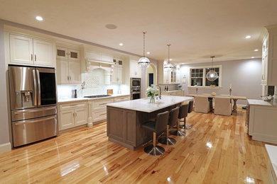 Eat-in kitchen - large galley light wood floor and beige floor eat-in kitchen idea in Boston with an undermount sink, beaded inset cabinets, white cabinets, quartz countertops, multicolored backsplash, porcelain backsplash, stainless steel appliances and an island