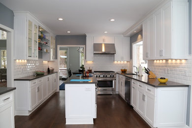 Large trendy galley dark wood floor and brown floor kitchen photo in New York with shaker cabinets, white cabinets, white backsplash, subway tile backsplash, stainless steel appliances, an island, an undermount sink and solid surface countertops