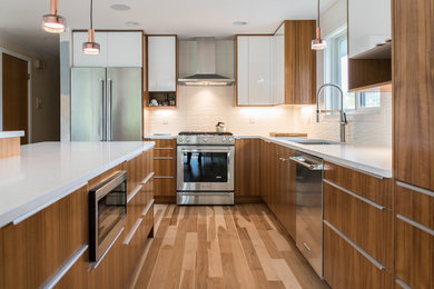 Inspiration for a mid-sized beach style l-shaped eat-in kitchen in Seattle with an undermount sink, flat-panel cabinets, quartz benchtops, white splashback, porcelain splashback, stainless steel appliances, light hardwood floors and with island.
