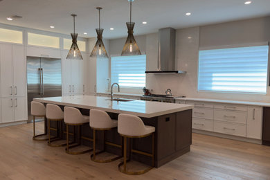 Eat-in kitchen - mid-sized transitional l-shaped medium tone wood floor eat-in kitchen idea in Miami with a single-bowl sink, shaker cabinets, white cabinets, quartz countertops, white backsplash, quartz backsplash, stainless steel appliances, an island and white countertops