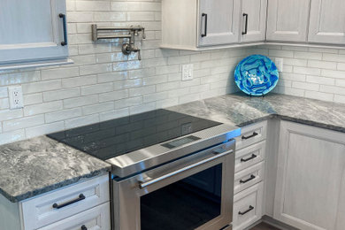 Example of a mid-sized classic u-shaped light wood floor and brown floor eat-in kitchen design in Cleveland with an undermount sink, recessed-panel cabinets, white cabinets, quartzite countertops, white backsplash, porcelain backsplash, stainless steel appliances, an island and gray countertops