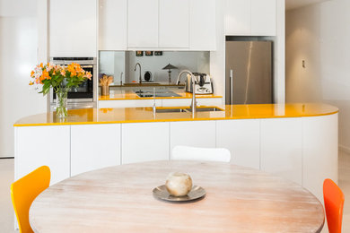 Design ideas for a small contemporary l-shaped open plan kitchen in Perth with an undermount sink, flat-panel cabinets, yellow cabinets, quartz benchtops, metallic splashback, glass sheet splashback, stainless steel appliances and with island.