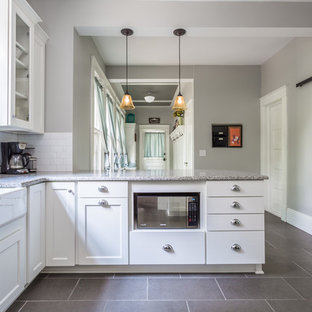 Idée de décoration pour une arrière-cuisine craftsman en U avec un évier de ferme, un placard à porte shaker, des portes de placard blanches, un plan de travail en granite, une crédence blanche, une crédence en carrelage métro, un électroménager en acier inoxydable, un sol en carrelage de porcelaine et une péninsule.